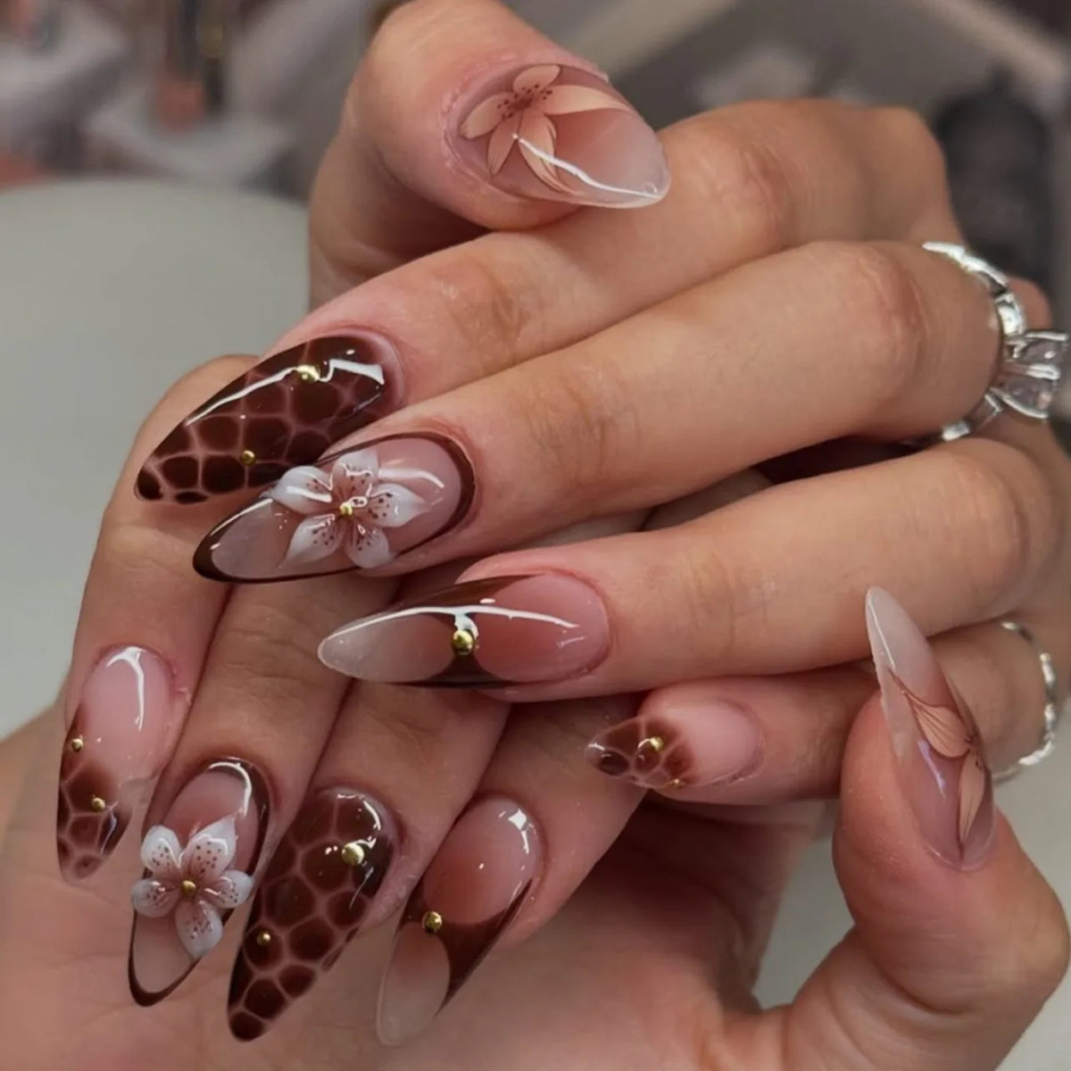 Decorative floral and embellished nail designs shown on hands